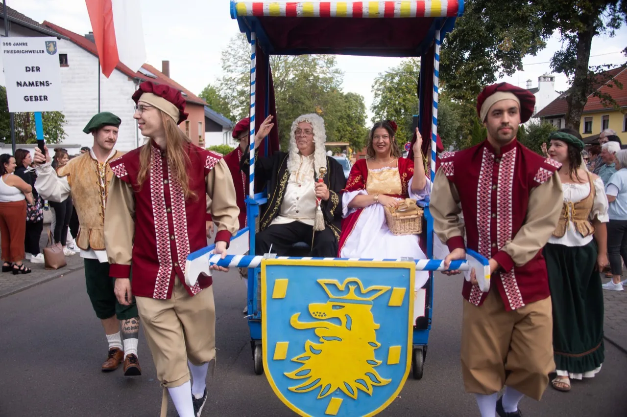 Eine historisch gekleidete Gruppe zieht mit einem blau-gelben Wappenwagen durch Friedrichweiler.